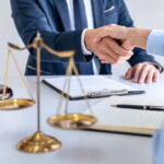 Poignée de main chaleureuse entre un conseiller juridique et un entrepreneur pour valider une création entreprise, avec une balance de la justice sur la table