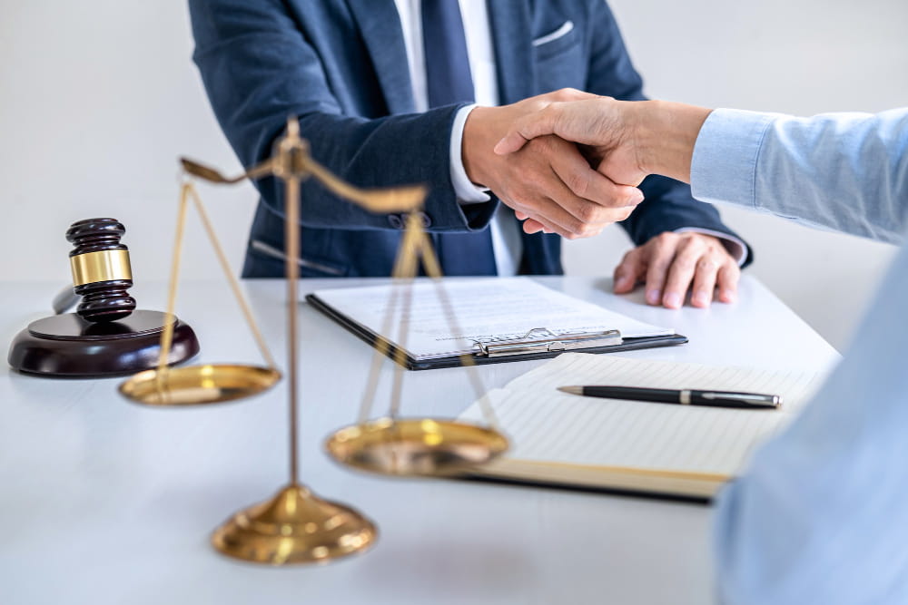 Poignée de main chaleureuse entre un conseiller juridique et un entrepreneur pour valider une création entreprise, avec une balance de la justice sur la table
