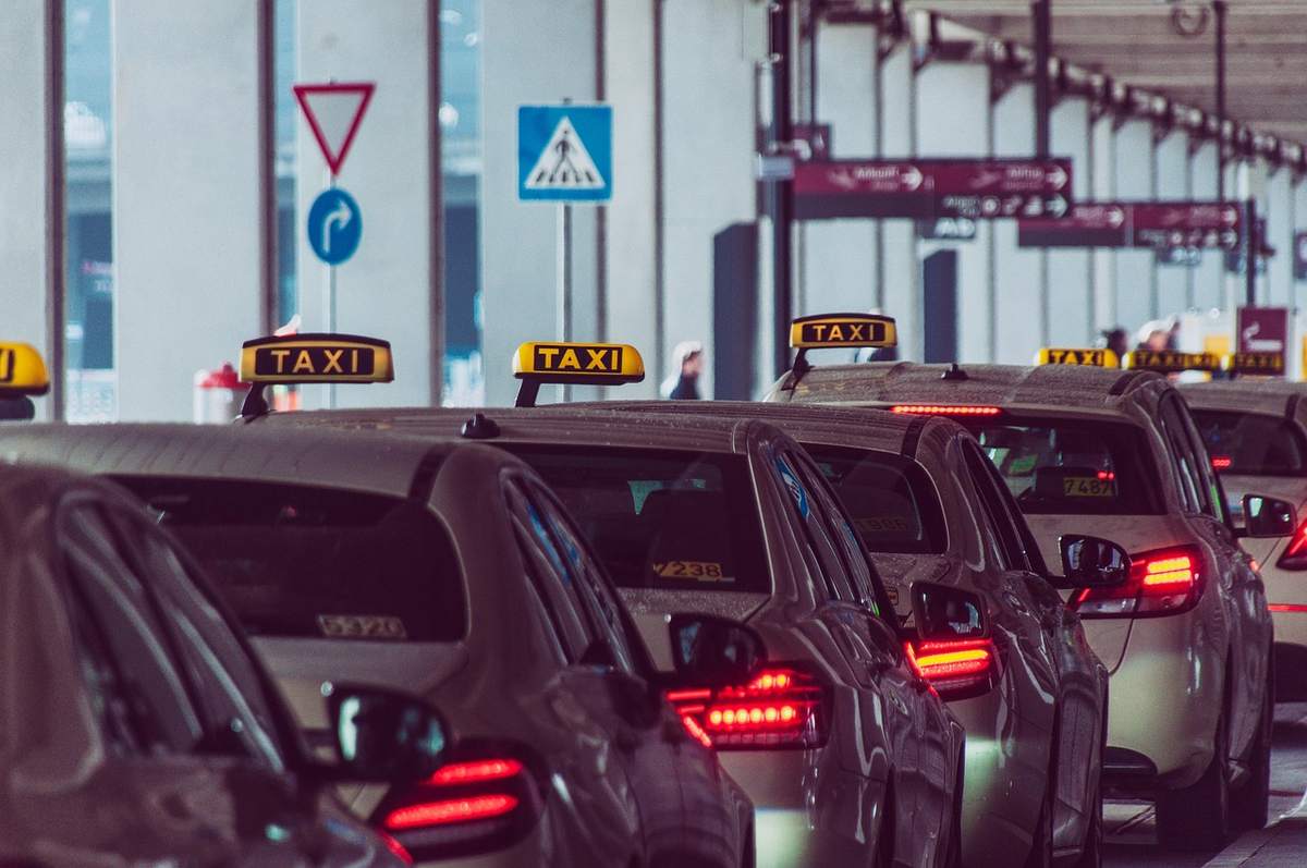 File de taxis devant un édifice, feux arrière allumés, panneaux de signalisation visibles File de taxis devant un édifice, feux arrière allumés, panneaux de signalisation visibles