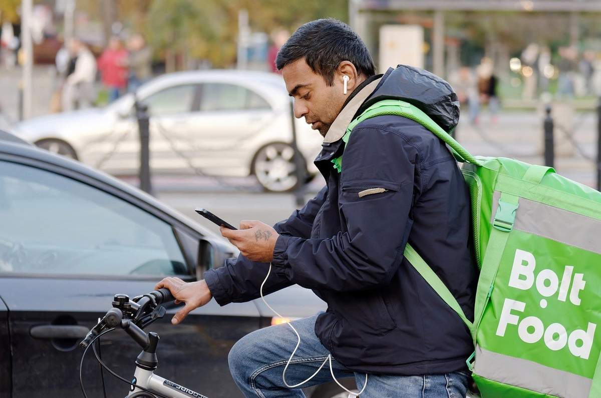 Homme cycliste avec téléphone et sac Bolt Food, en ville Homme cycliste avec téléphone et sac Bolt Food, en ville