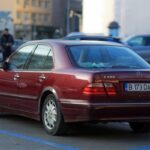 Mercedes berline rouge garée sur un parking urbain avec immeubles en arrière-plan