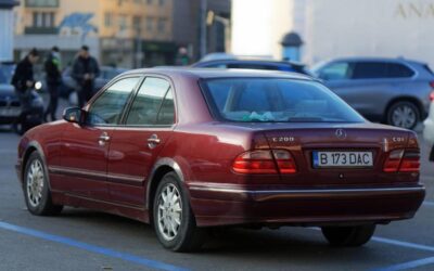 Mercedes berline rouge garée sur un parking urbain avec immeubles en arrière-plan