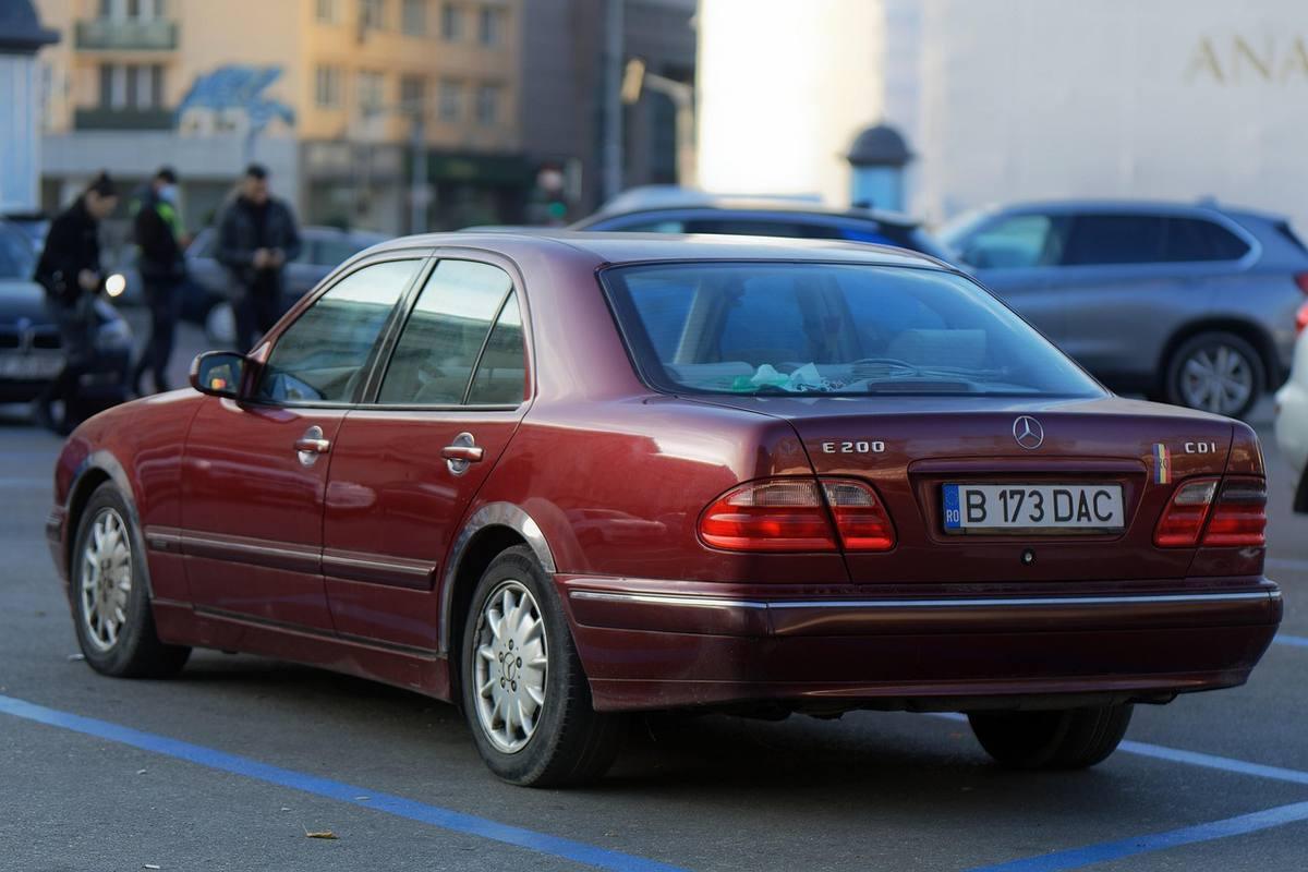 Mercedes berline rouge garée sur un parking urbain avec immeubles en arrière-plan