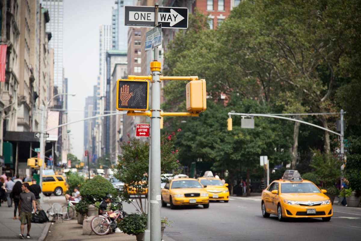 Taxis jaunes circulent sur une avenue bondée avec piétons et panneaux