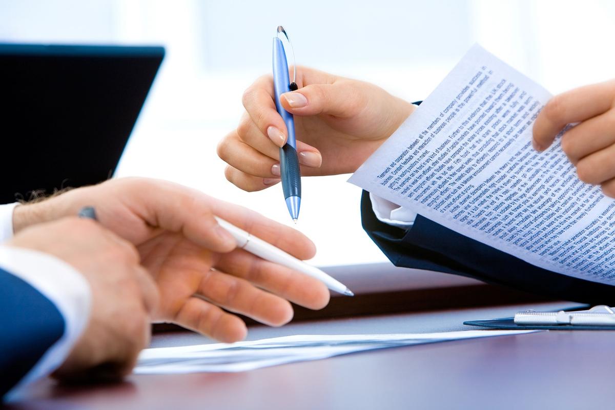 Deux personnes à un bureau, l'une tenant un stylo, signant un document professionnel