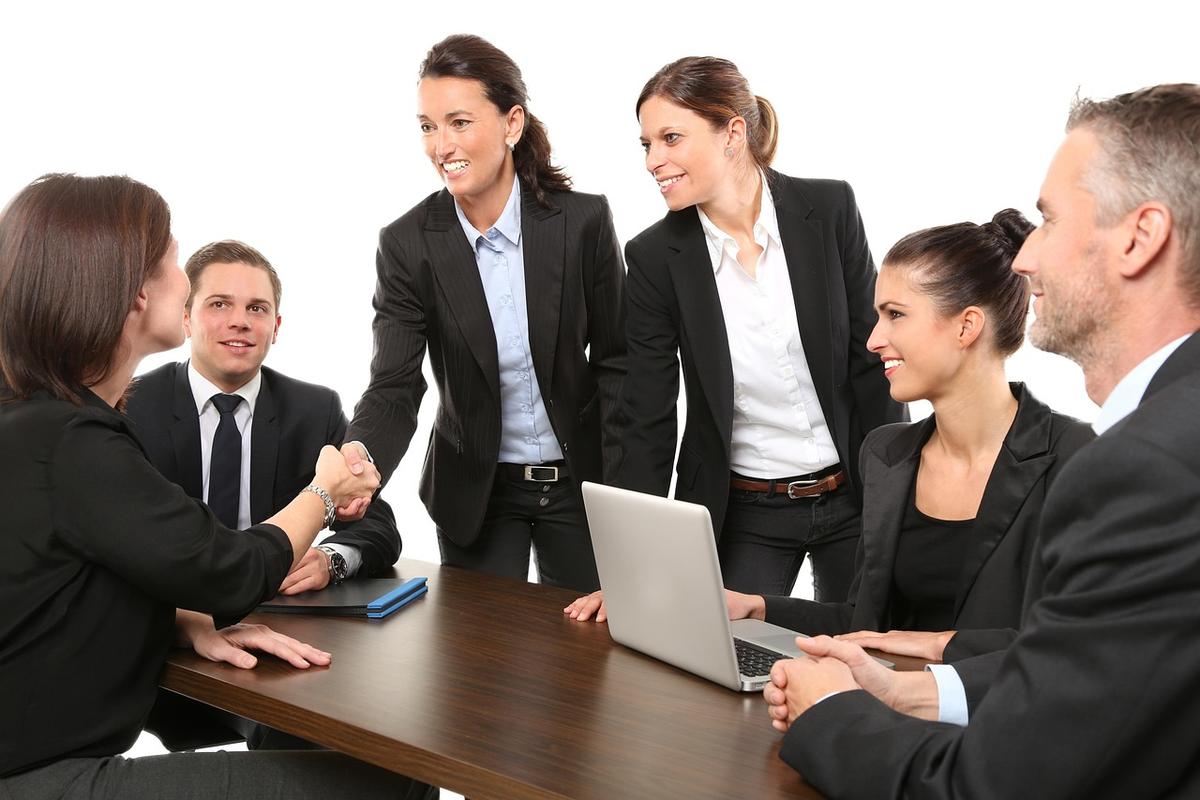 Six professionnels en costume discutent autour d'une table avec ordinateur portable, dans un cadre de réunion d'affaires
