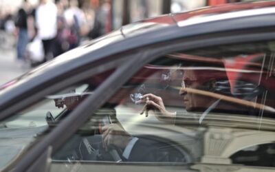 Un homme dans une voiture, main levée, reflet de la rue