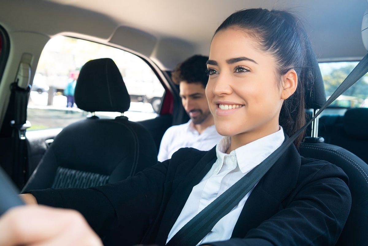 Une femme en costume conduit une voiture avec un passager à l'arrière