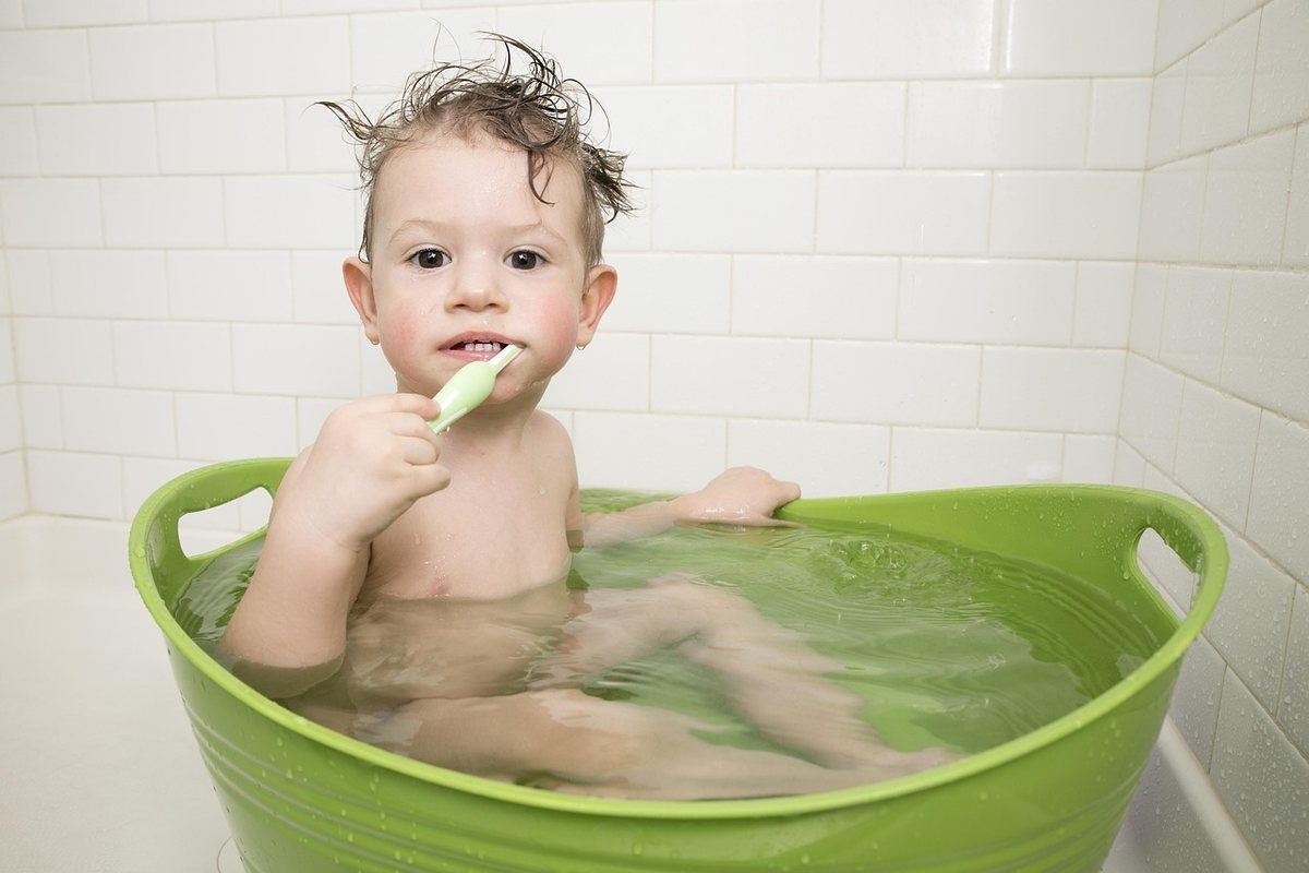Enfant en train de se brosser les dents dans une baignoire verte Enfant en train de se brosser les dents dans une baignoire verte