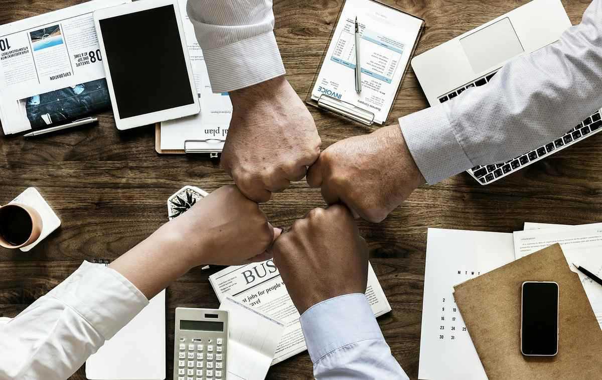 Quatre mains jointes au-dessus d'un bureau avec ordinateurs, documents et fournitures de travail Quatre mains jointes au-dessus d'un bureau avec ordinateurs, documents et fournitures de travail
