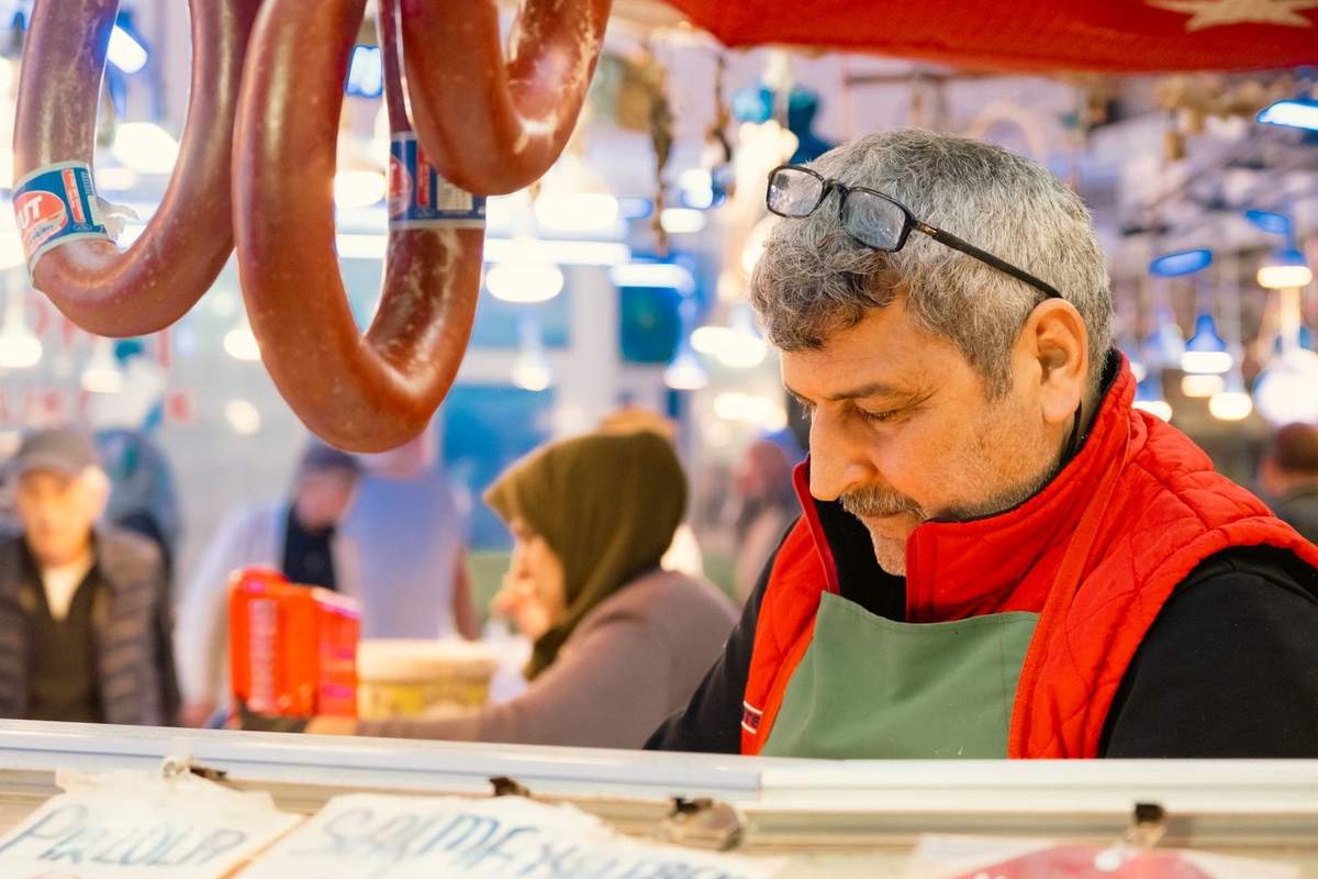 Homme en rouge devant étal de saucisses, marché bondé en arrière-plan