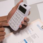 Mains saisissant des chiffres sur une calculatrice, documents et feuilles sur une table