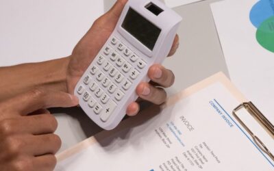 Mains saisissant des chiffres sur une calculatrice, documents et feuilles sur une table