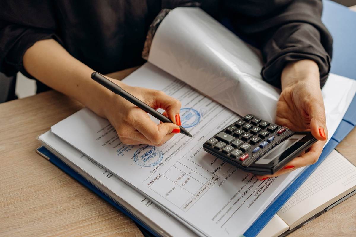 Une personne utilise une calculatrice et écrit dans un livre ouvert sur une table Une personne utilise une calculatrice et écrit dans un livre ouvert sur une table