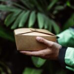 Main portant un carton brun dans un cadre de végétation dense