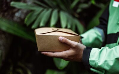 Main portant un carton brun dans un cadre de végétation dense