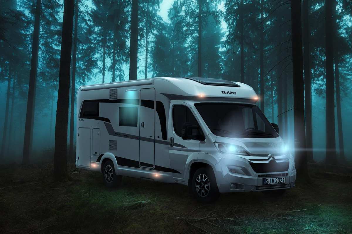 Une fourgonnette camper blanche aux phares allumés dans une forêt brumeuse nocturne Une fourgonnette camper blanche aux phares allumés dans une forêt brumeuse nocturne