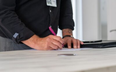 Homme écrivant sur une table avec un stylo, dossier et porte visibles