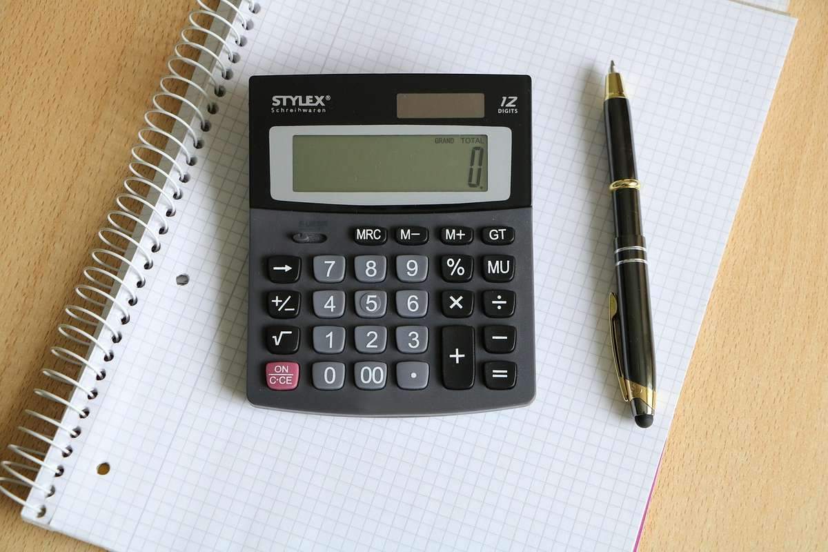 Calculatrice de bureau noire affichant zéro sur carnet quadrillé spiralé avec stylo Calculatrice de bureau noire affichant zéro sur carnet quadrillé spiralé avec stylo