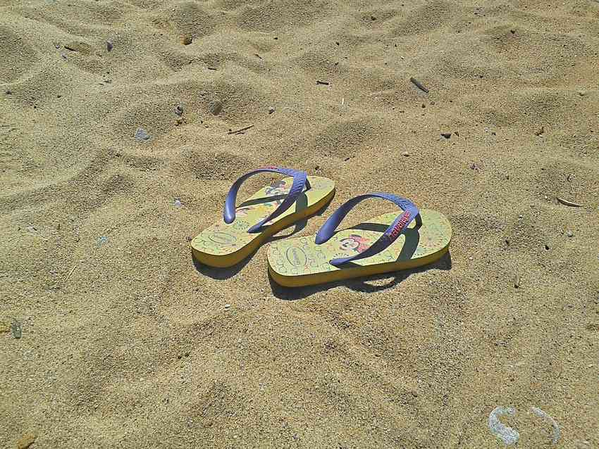 Tongs et sandales posées sur un sol en bois.