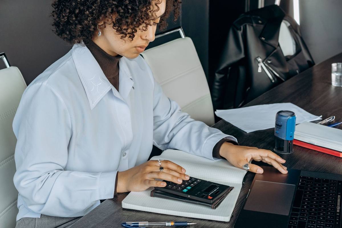 Femme en blouse blanche utilisant une calculatrice sur une table avec des documents et un ordinateur portable