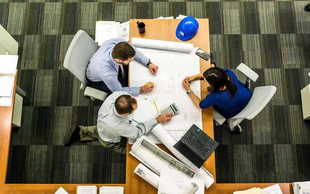 Trois collaborateurs étudient des plans sur une table de bureau Trois collaborateurs étudient des plans sur une table de bureau